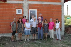 A group from the Noah Association in front of an orange-red brick shell with white window frames and a white door, known as the 'House of Smiles'.